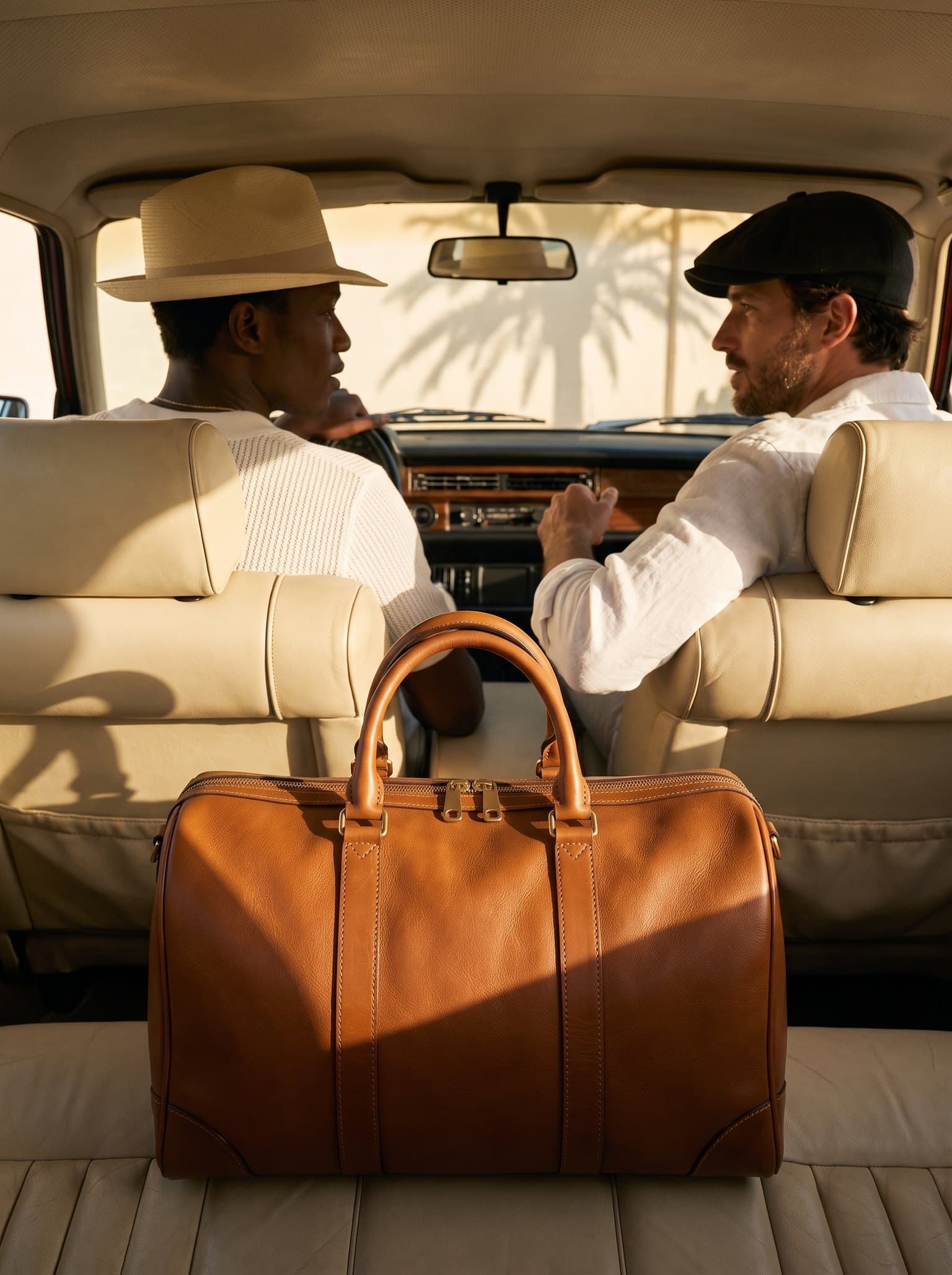 A cognac Vantier Holdall on the back seat of a car, two friends up front in the sun